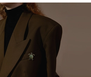 Detail of vintage turtle brooch with emerald enamel on a dark brown blazer lapel