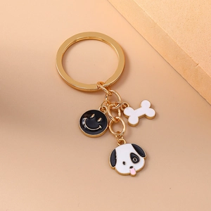 Golden metal keychain featuring cartoon dog, bone, and black smiley face charms