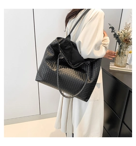 Detail of a black woven oversized tote bag worn with an elegant beige trench coat