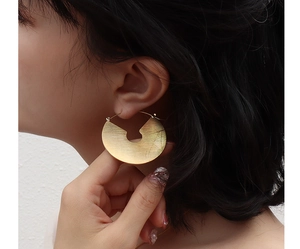 Close-up of a model wearing large golden crescent hoop earrings with brushed texture
