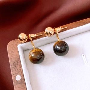Macro shot of 18k gold plated tiger eye stone drop earrings on a silk background