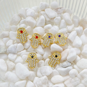 Detail of golden Hamsa Hand charms with inlaid zircon and colorful center stones on stones