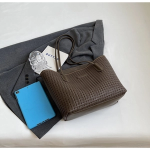 Top view of dark brown woven tote bag on bed with modern lifestyle accessories
