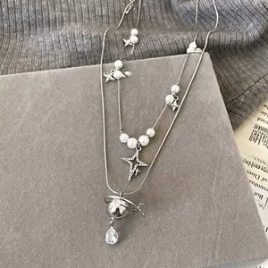 Close-up of double-layer necklace with Saturn pendant, star pearl, and zircon teardrop