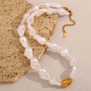 Détail d'un collier de perles baroques avec bille dorée sur une pierre texturée