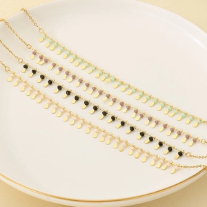 Gold-plated collar necklaces with oval tassels and colorful beads on a white ceramic plate