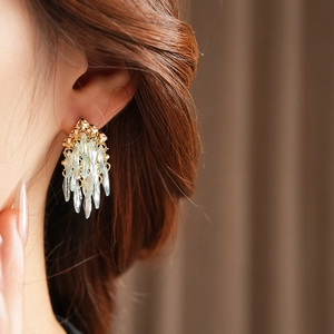 Gros plan de boucles d'oreilles franges dorées avec cristaux bleus sur l'oreille du modèle