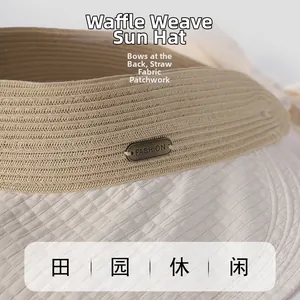Detail of straw and waffle fabric texture on a wide brim sun hat with metal fashion tag