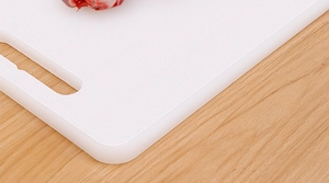 Close-up of a white rectangular plastic cutting board with anti-slip texture and handle