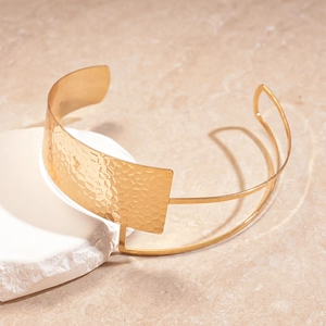 Close-up of golden wide cuff bracelet with hammered texture on beige marble background