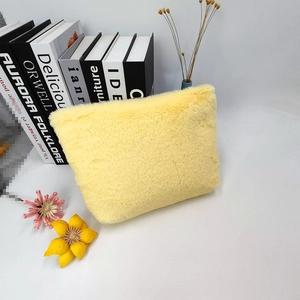 Close-up of pale yellow plush makeup bag with soft faux fur texture next to books