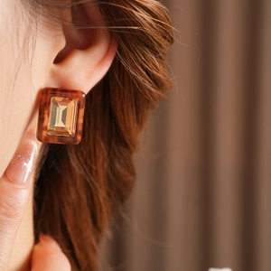 Close-up of square amber resin earring with faceted gemstone on a model's ear