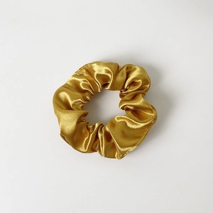 Detailed view of the smooth golden satin texture and folds of the elastic scrunchie