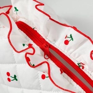 Gros plan sur le zip rouge d'une trousse à maquillage blanche matelassée à motif cerise