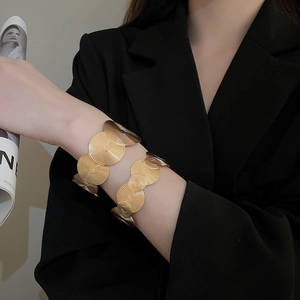 Detail of gold-tone geometric open cuff bracelet with concentric texture on a model