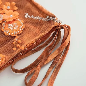 Detail of orange mesh bikini skirt featuring sequins, floral embroidery, and pearl accents