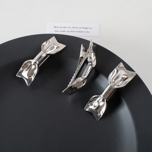 Detail view of silver geometric metal hair clips with abstract shapes on a black tray