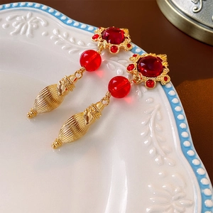 Dettaglio di orecchini vintage dorati con gemme rosse e pendenti a goccia su un piatto decorato
