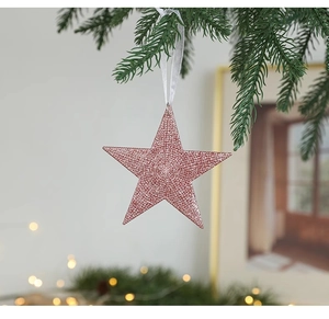 Close-up of pink glitter star ornament hanging on green pine branch for Christmas
