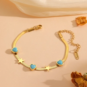 Bracelet chaîne serpent dorée avec cœurs bleus et étoiles dorées sur tissu beige