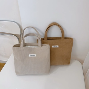 Detail of camel and cream corduroy tote bags showing the striped fabric and logo label