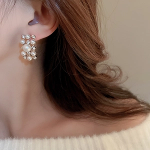 Close-up of model wearing gold vintage earrings with pearls and rhinestones on beige background