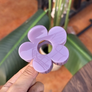 Détail d'une pince à cheveux fleur mauve clair au centre évidé tenue en main
