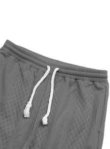 Détail de la taille du jogging jacquard gris foncé avec cordon blanc sur tissu gaufré