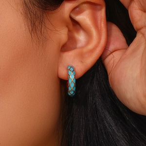 Macro view of blue enamel hoop earring with golden diamond grid pattern on model ear
