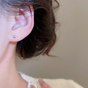 Close-up of minimalist 3mm gold ball stud earrings featuring a polished metal finish
