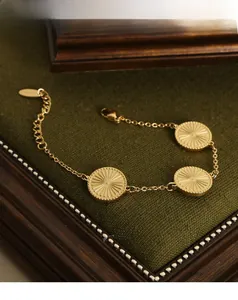 Detail of gold plated titanium bracelet with three sunburst texture round pendants