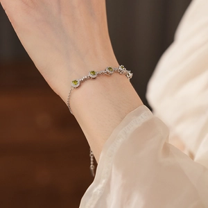 Close-up of elegant silver bracelet with round green stones and halo diamond setting