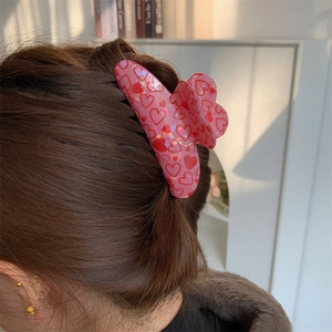 Pink hair claw clip with red heart patterns worn by a model in natural lighting