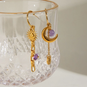 Detailed shot of celestial gold earrings with purple stones on textured glass edge
