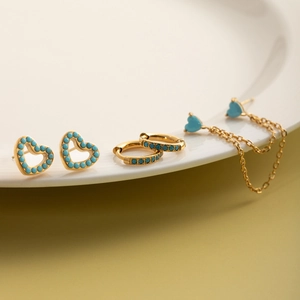 Detailset aus drei goldenen Ohrringen mit blauen Türkis-Herzsteckern und Kettenhängern