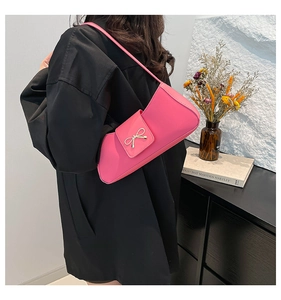 Detail shot of the pink baguette bag with a decorative gold bow and elegant PU leather