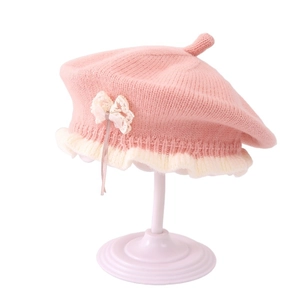 Pink knitted baby beret with white lace bow and ruffled edges on display stand