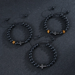 Matte black tiger eye beaded bracelets with metallic cross charms on textured background