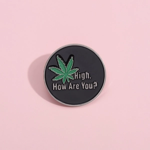 Round black enamel brooch pin featuring a green maple leaf and fun greeting text