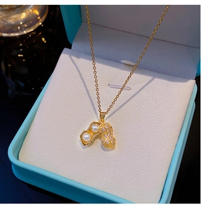 Gros plan du pendentif cacahuète doré avec perle et zircon sur un écrin à bijoux bleu