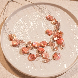 Detail of layered beaded necklace with pink shells in a white decorative tray