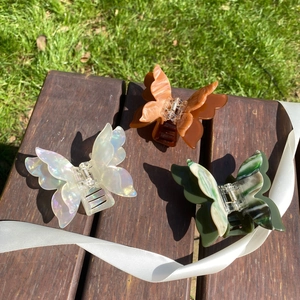 Close-up of three acetate butterfly hair claws in white, amber, and green on wood