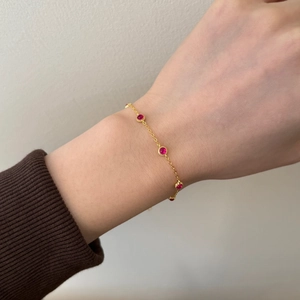 Macro detail of a fine gold chain bracelet featuring a round inlaid red gemstone
