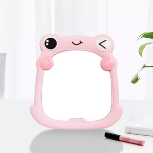 Pink frog desktop makeup mirror on a table with cosmetic accessories and green plant background