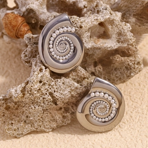 Close-up of conch shell stud earrings with white pearls on a coral stone display