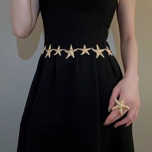Detailansicht einer goldenen Seestern-Taillenkette und eines großen Rings am Kleid