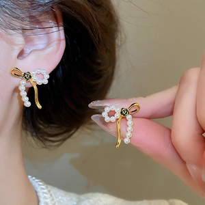 Detail view of 18k gold plated pearl bow earrings featuring black flower design on model