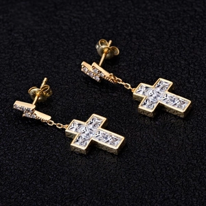 Makroaufnahme goldener Kreuzohrringe mit Zirkoniasteinen auf schwarzem Leder