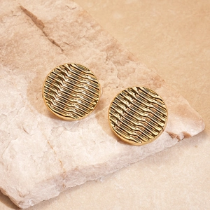 Detail of golden wavy round stud earrings resting on a minimalist beige stone background