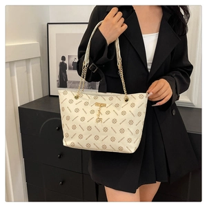 Vintage tote bag with monogram pattern and gold chain strap worn by a model in black blazer